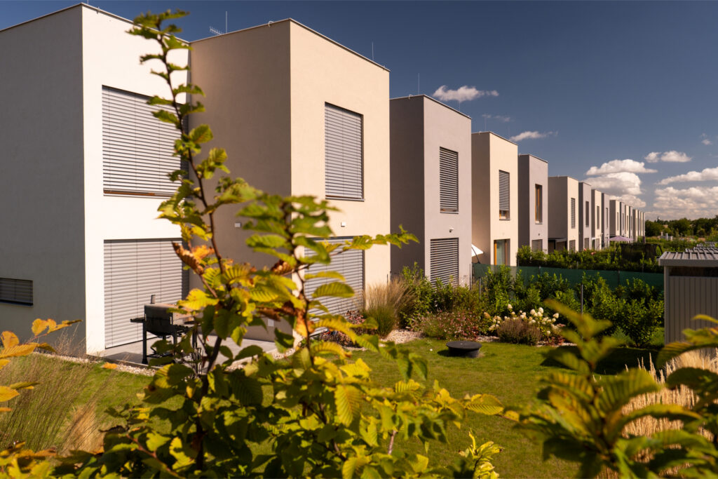 Řada moderních nízkoenergetických domů se soukromými zahradami a předokenním stíněním za slunečného dne.