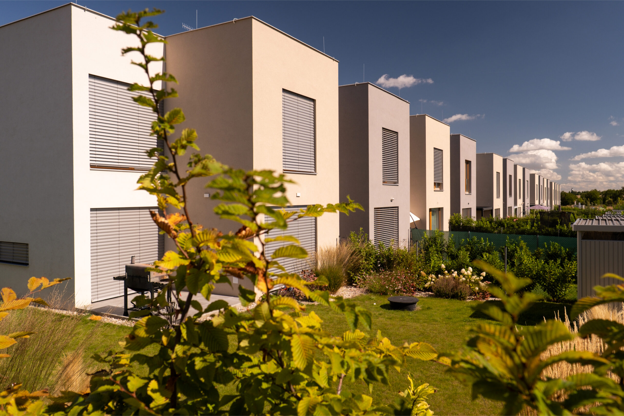 Řada moderních nízkoenergetických domů se soukromými zahradami a předokenním stíněním za slunečného dne.