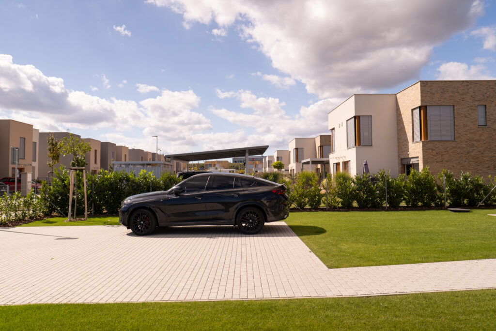 Moderní rodinné domy v projektu Domy Bílý Vrch s parkovacím stáním a upraveným trávníkem, zaparkované auto v klidné rezidenční ulici.