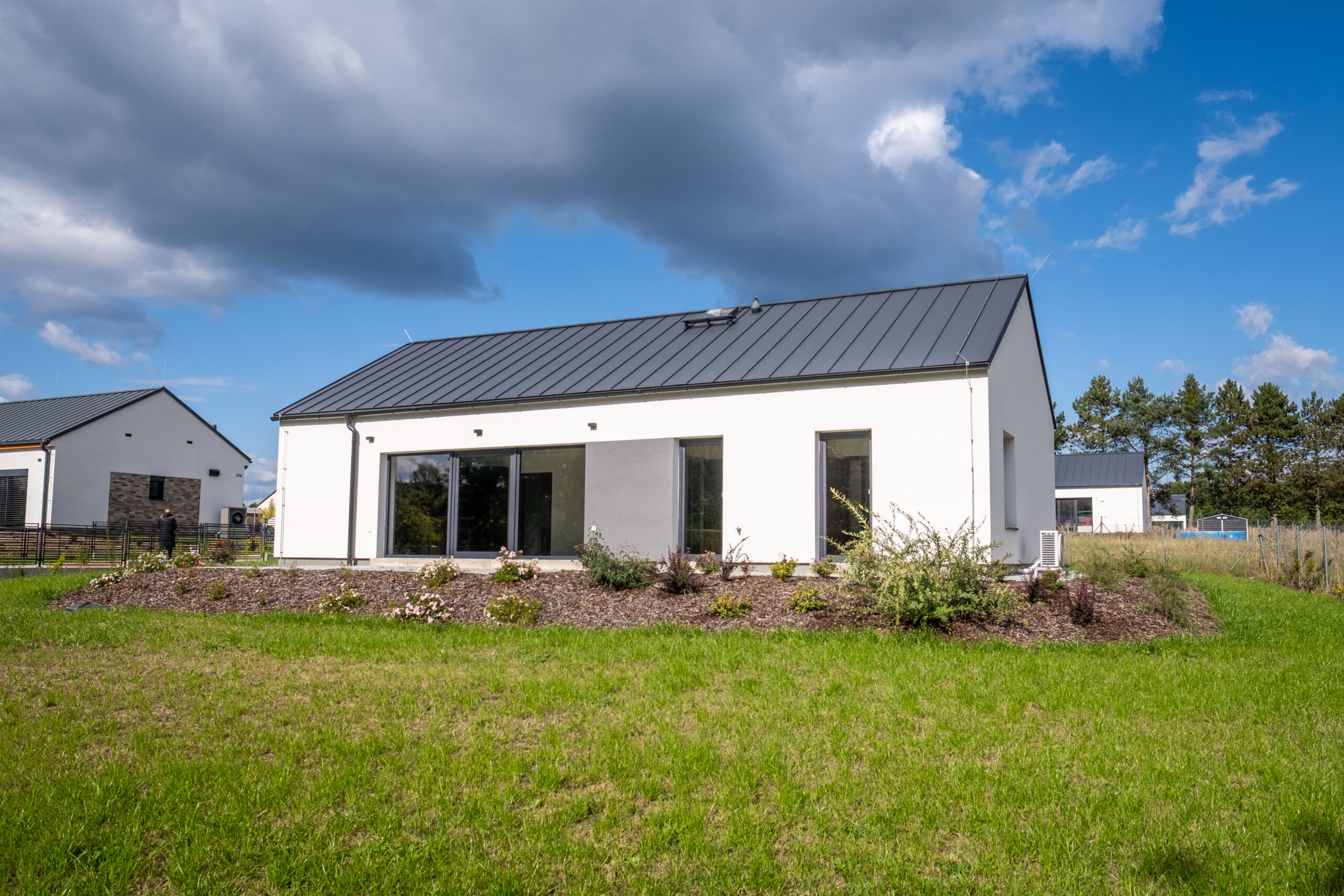 Moderní přízemní rodinný dům s velkými francouzskými okny, sedlovou plechovou střechou a zahradou v klidné rezidenční lokalitě.