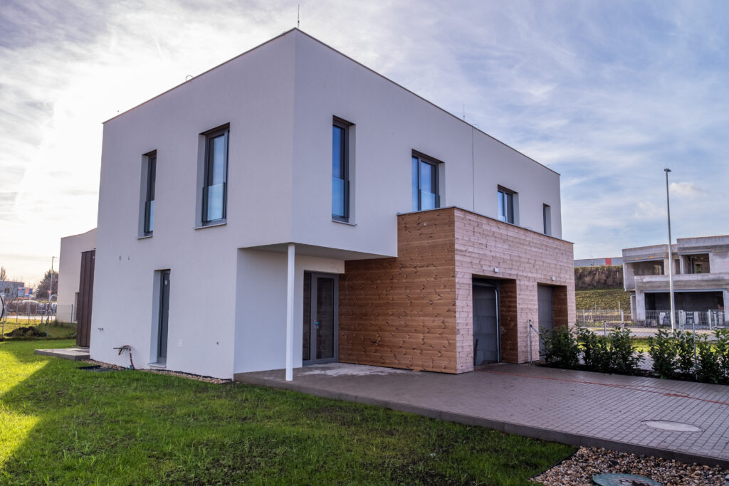 Moderní dvojdům s bílou fasádou, dřevěným obkladem a terasou u zahrady