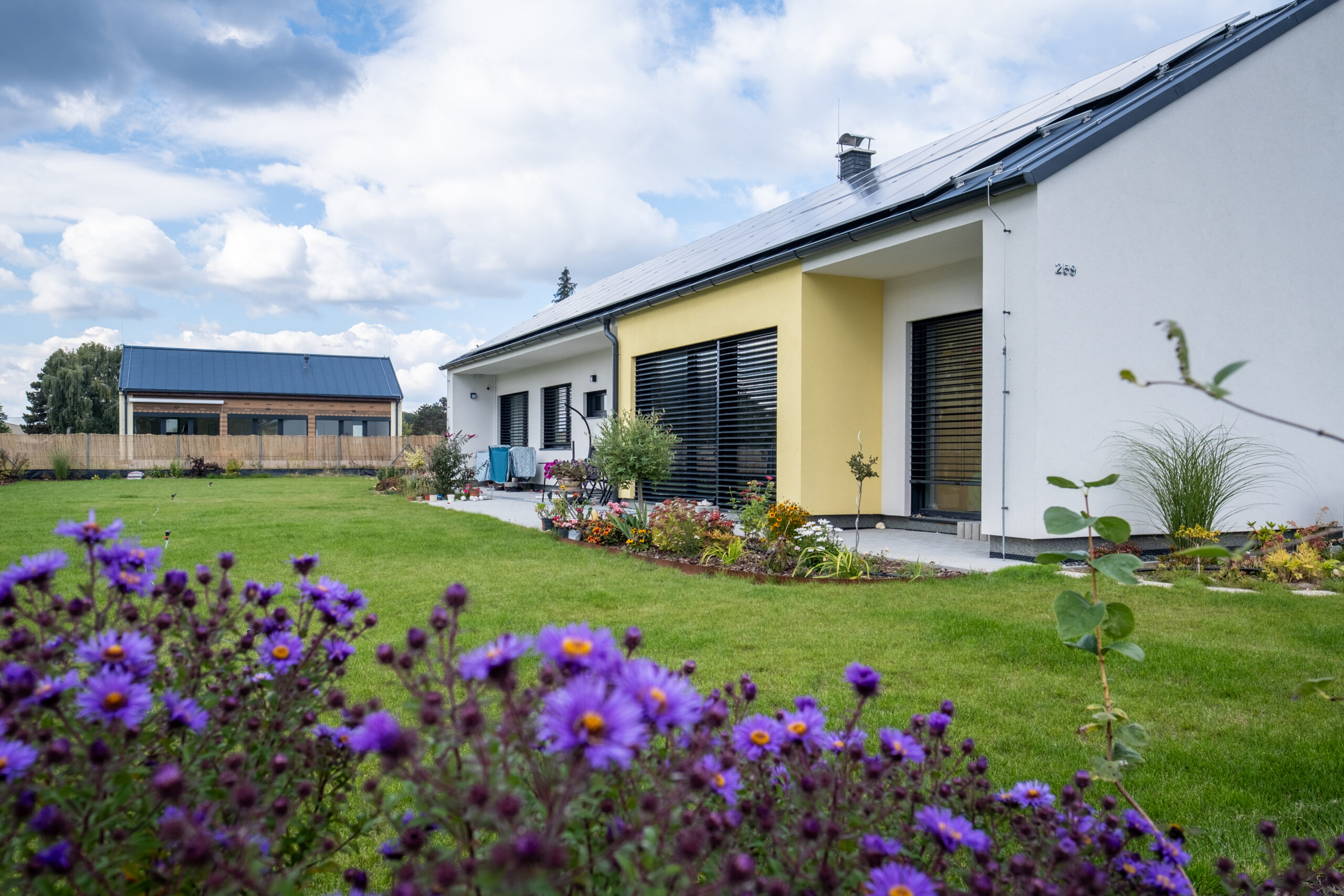 Moderní novostavba rodinného domu s fotovoltaikou na střeše a venkovním stíněním. Ukázka úsporného bydlení s nízkými provozními náklady.