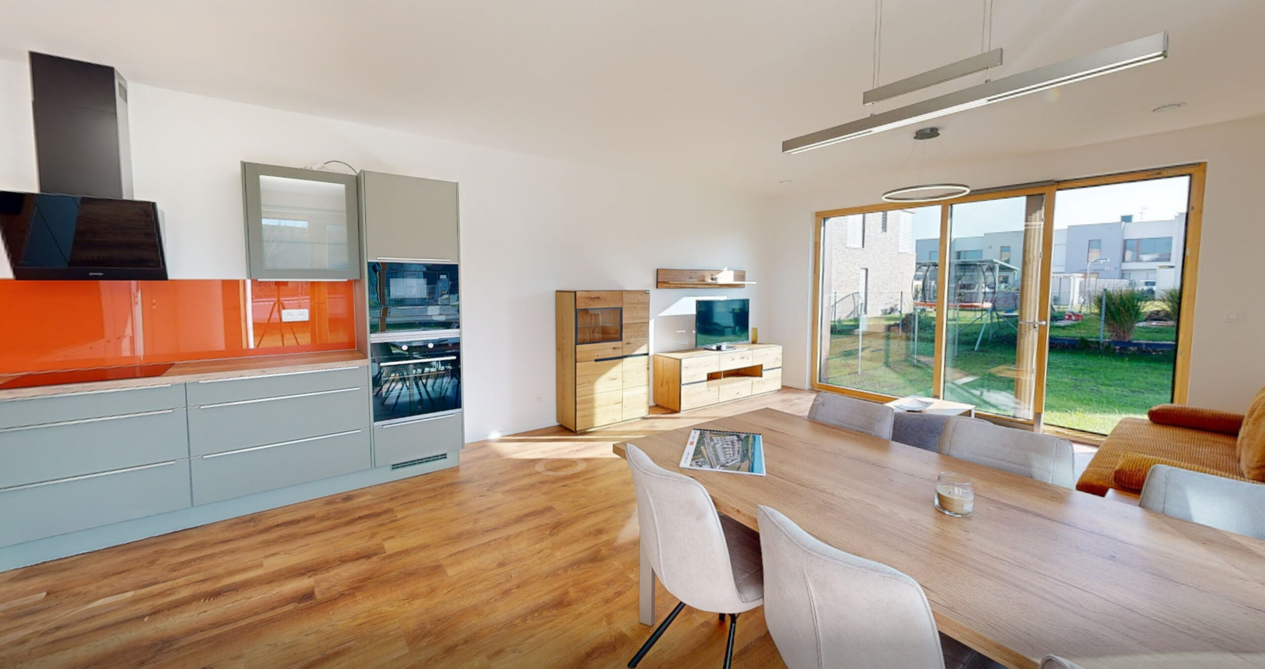 Světlý otevřený obývací pokoj s kuchyní a jídelnou v novostavbě. Velké prosklení do zahrady a moderní interiérový design.